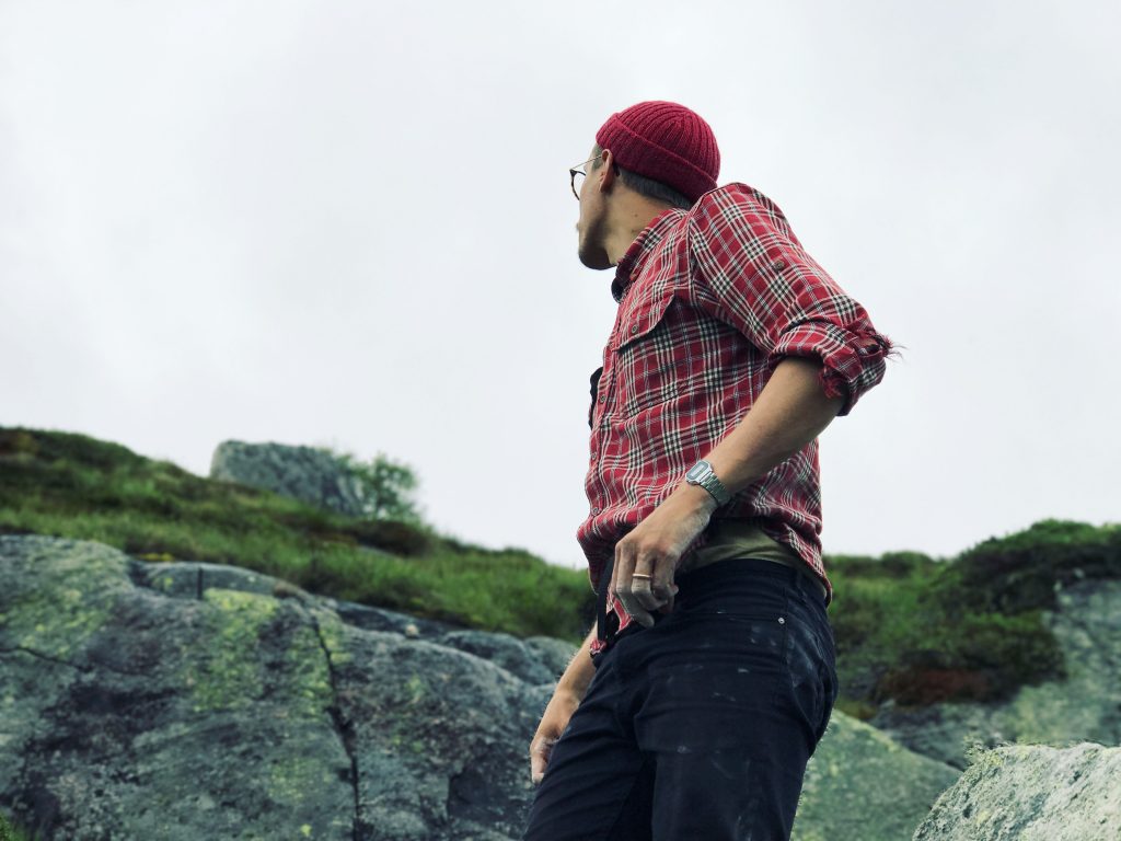 A man wearing a red handknitted cap looking across a mountain.